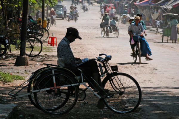 庶民の乗り物の代表といえば、自転車の横に背中合わせの座席を据えたサイカー(サイドカーの略)であろうか。
新聞や雑誌を読んで客待ちをする運転手の姿をよく見かけた。(エーヤワディー地域・パテェイン、2003年)(c) 筆者撮影